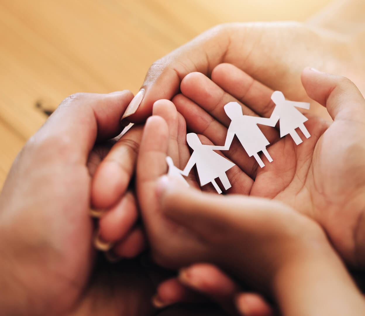 An image of hands gathered around a paper cutout of a family.