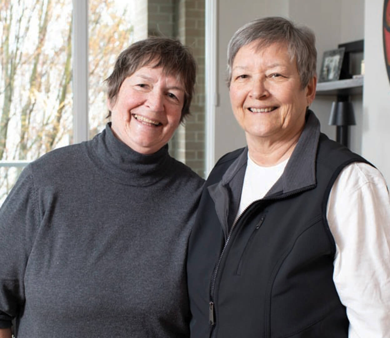 Two women donors standing in their living room smile at the camera.