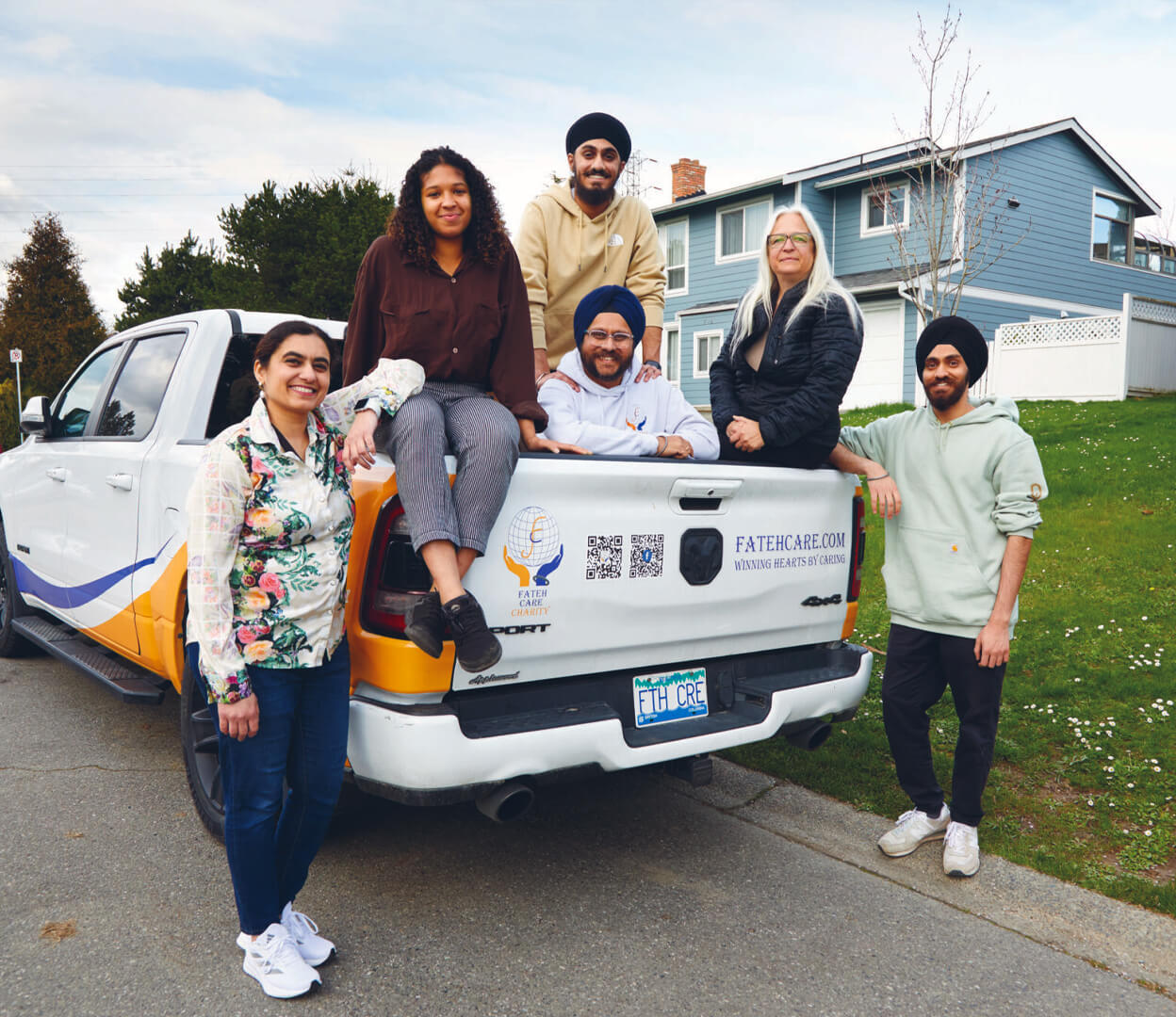 A group of people are smiling while sitting in the back of a pickup truck from Fateh Care Charity.