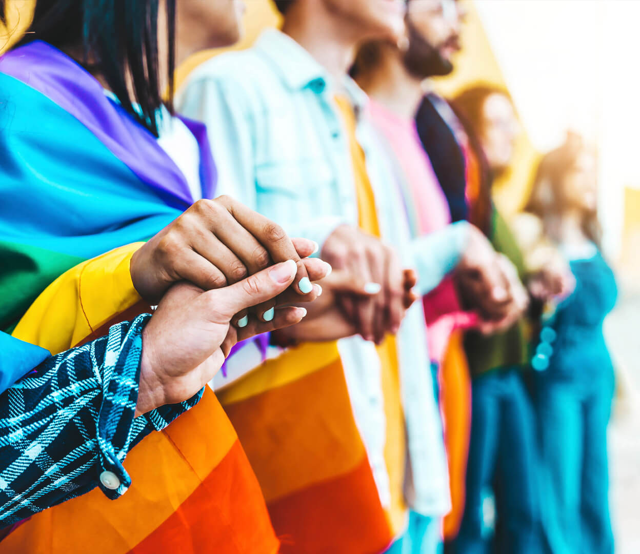A group of diverse people with inclusive flags hold hands.