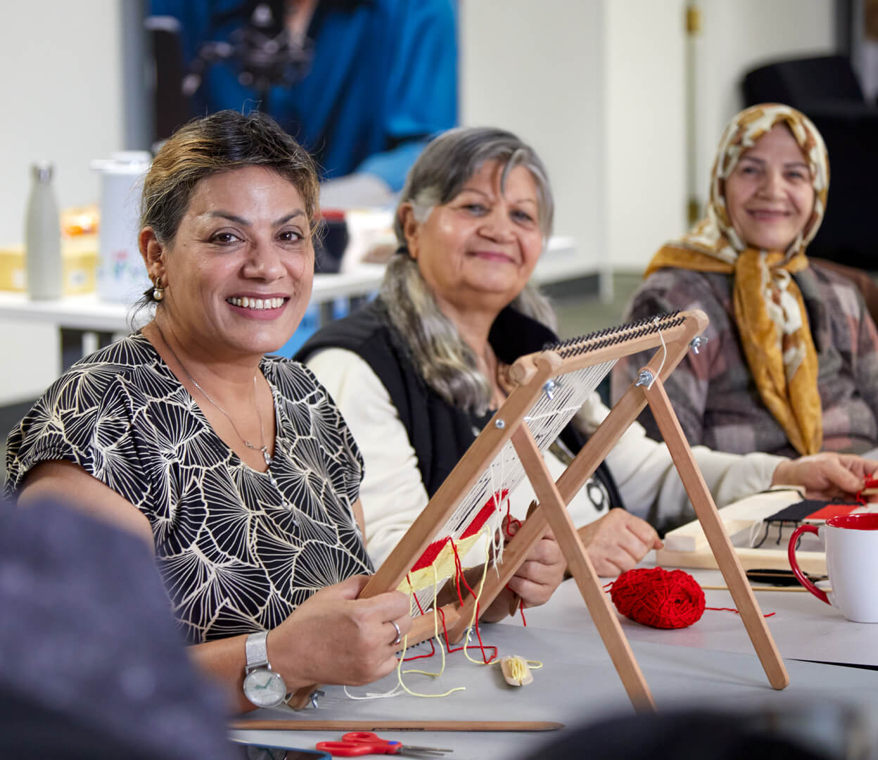 Three women smile at the camera while attending a weaving workshop at the Inter-cultural Association of Greater Victoria.