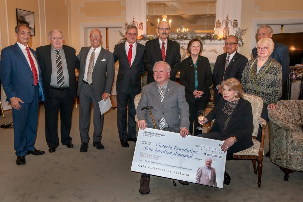 Mel Cooper poses for a photo with various members of the community: Gordy Dodd, Wayne Cooper, Dale Boniface, Randall Mang, Dick Auchenleck, Sandra Richardson, Naz Rayani, Iain Harris (hidden). Mel and Carmella Cooper in foreground.