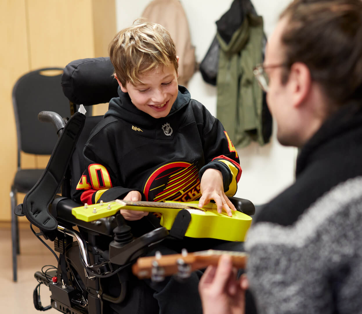A young boy in a wheelchair plays a ukulele while participating in music therapy at the Victoria Conservatory of Music.
