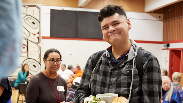 A smiling young person looks at the camera while enjoying lunch at the Victoria Native Friendship Centre.