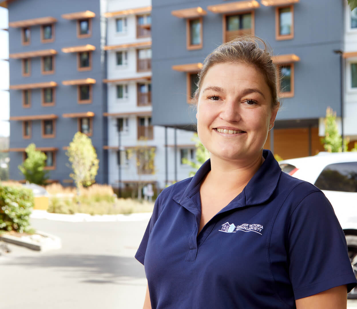 A woman from the Greater Victoria Housing Society stands proudly in front of a newly completed housing project.