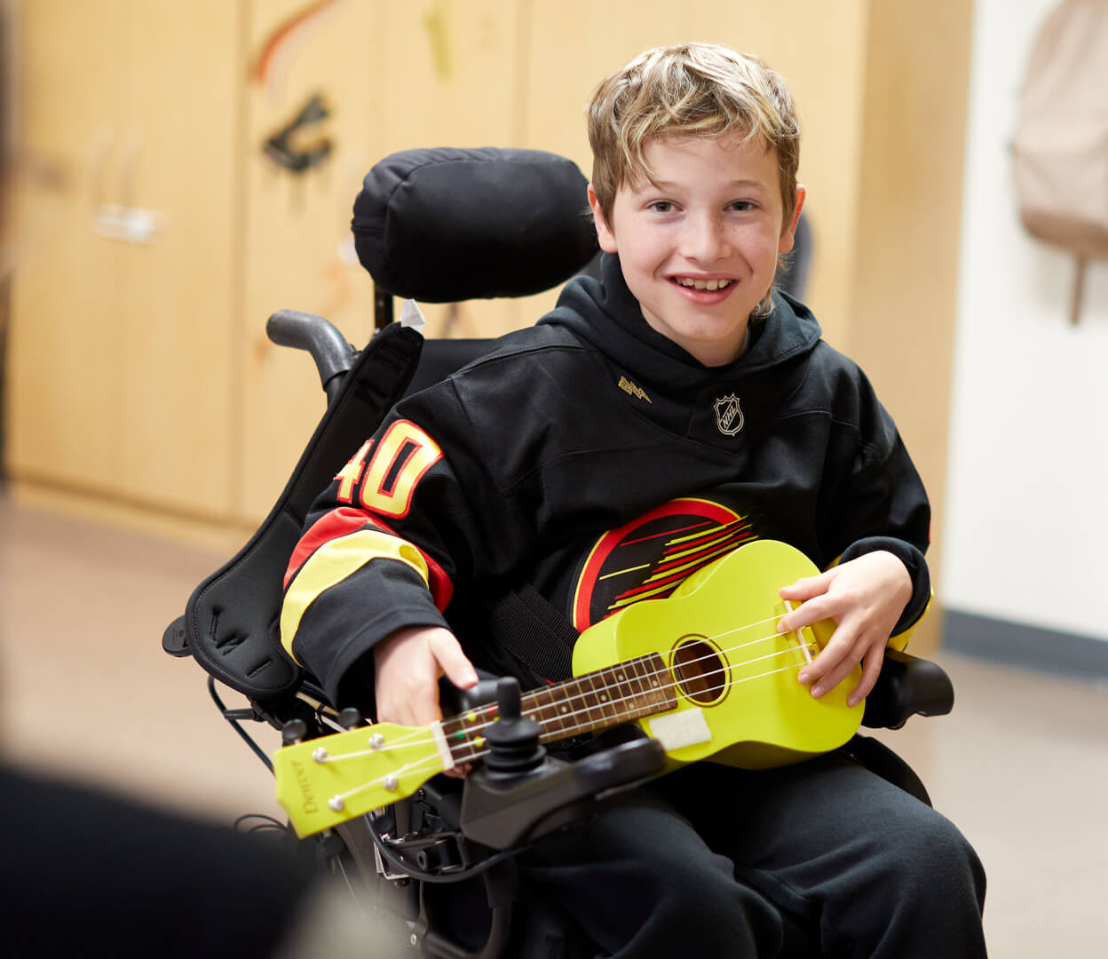 A young boy in a wheelchair plays a ukulele while participating in music therapy at the Victoria Conservatory of Music.
