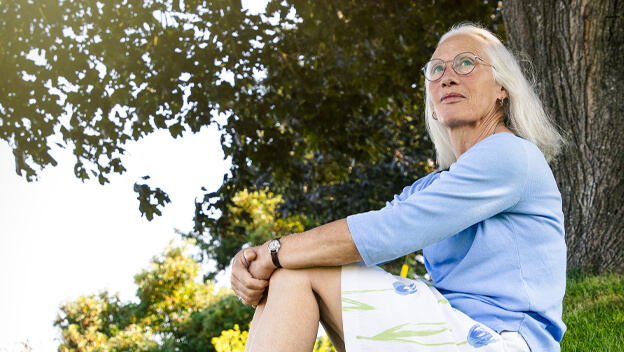 A woman is sitting on a grassy hill while looking thoughtful.