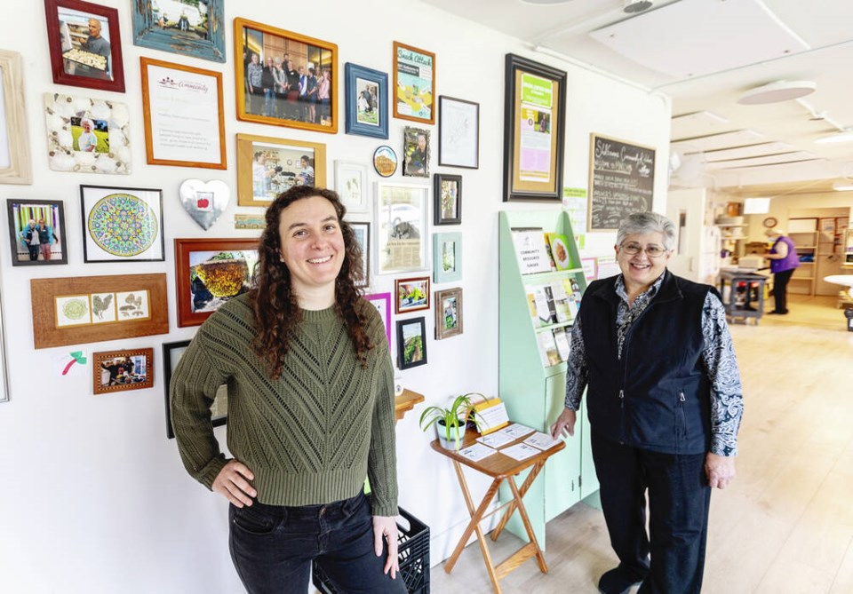 Kim Cummins, left, and Clarice Dilman pose for a photo in front of a wall full of historical photos at the Shelborne Community Kitchen